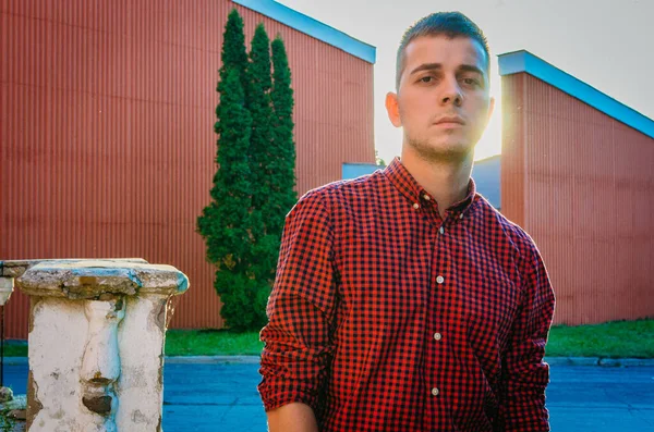Portrait of a pensive young guy in a red tart shirt on a background of buildings