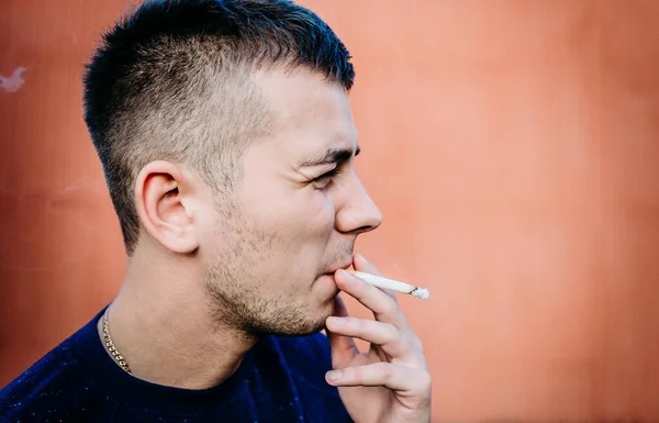 Duvarın yanında sigara içen bir gencin portresi.