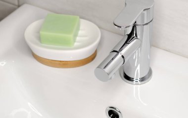 Banyodaki beyaz lavaboda krom musluğun yanında sabun var.