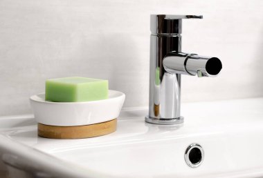 Banyodaki beyaz lavaboda krom musluğun yanında sabun var.