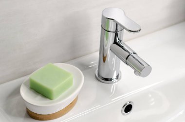 Banyodaki beyaz lavaboda krom musluğun yanında sabun var.