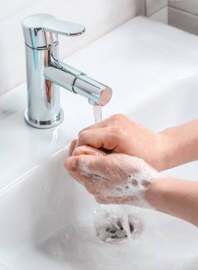 Banyoda sabunlu suyla el yıkama. Genç bir adam ellerini sabunla yıkıyor. Koronavirüsle mücadele.