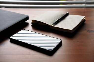 Bilgisayar, cep telefonu ve defter eski ahşap bir masanın üzerinde.