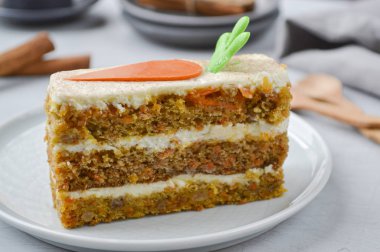 Ulusal Havuçlu Kek Günü. Havuçlu kek, krem peynirli krem şantili. Hafif ahşap arka planda çikolatalı havuçla süslenmiş. Yakın çekim, üst görünüm