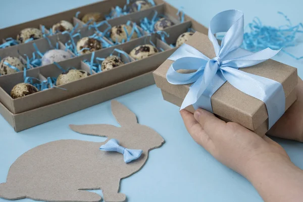 Child gives a gift box . Close-up of a child\'s hand and with a gift box on a blue background.  The concept of a gift for Easter. A box with Easter eggs and an Easter Bunny on a blue background.   Holidays, the present, the concept of childhood. top v