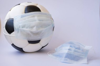 Soccer ball in a medical mask on a light background. Crown protection against viruses and bacteria is discontinued. Cancellation of sporting events. Copy space clipart