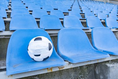 Boş stantların arkasında tıbbi maske takmış futbol topu. Tacın virüslerden ve bakterilerden korunması sona erer. Spor etkinliklerinin iptali. Açık bir stadyumda sıra sıra sandalye. Boşluğun bir kopyası.