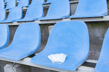 A medical mask is lying on a stadium chair. Empty stands.Protection of the crown from viruses and bacteria ceases. Cancellation of sporting events. Rows of chairs in an open stadium. A copy of the space. clipart