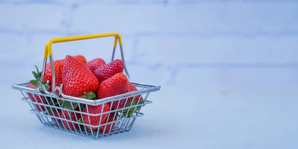 fresh strawberries with a shopping basket on a light background. advertising concept for fresh products.Self-service supermarket shopping basket with fresh strawberries. copy space
