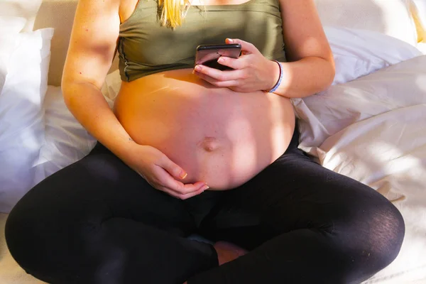 Těhotná při pohledu na telefon jedné ruky nad druhou pod přední pohled na břicho — Stock fotografie