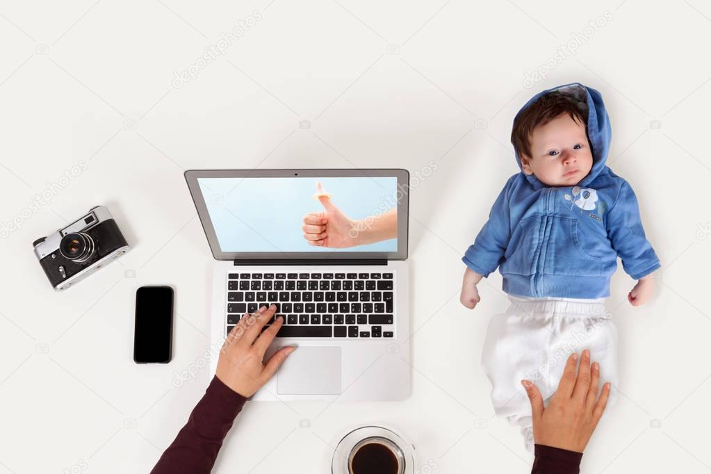 Mother holding baby while working on laptop. 