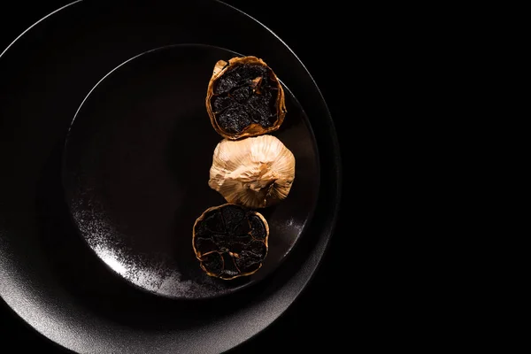 Black garlic on black plate. — Stock Photo, Image