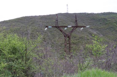 Demir direk uzun zamandır burada dikiliyordu. Yüksek voltajlı iletim hattı var. Tepede bir TV kulesi görülebilir. Direğin yanında, çimenler, ağaçlar ve dikenli çalılar.