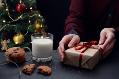 Genç Avrupalı kadın kırmızı kurdeleli yeni yıl hediyesini elinde tutuyor. Bir cam.