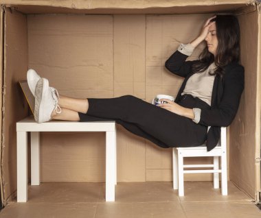 stressed out businesswoman sitting in cramped craton office, holding a coffee cup clipart