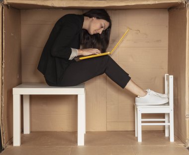 Genç, güzel bir iş kadını ofis karton kutusunda oturuyor, dizüstü bilgisayarla çalışıyor.