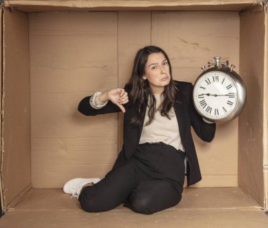 İş kadını elinde saatle karton bir ofiste oturuyor.