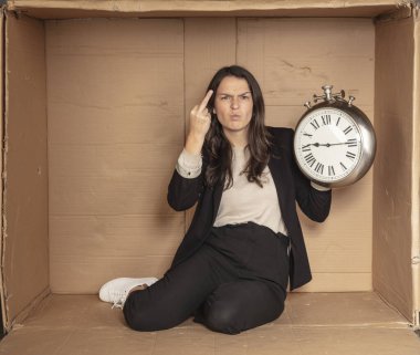 İş kadını elinde saatle karton bir ofiste oturuyor.