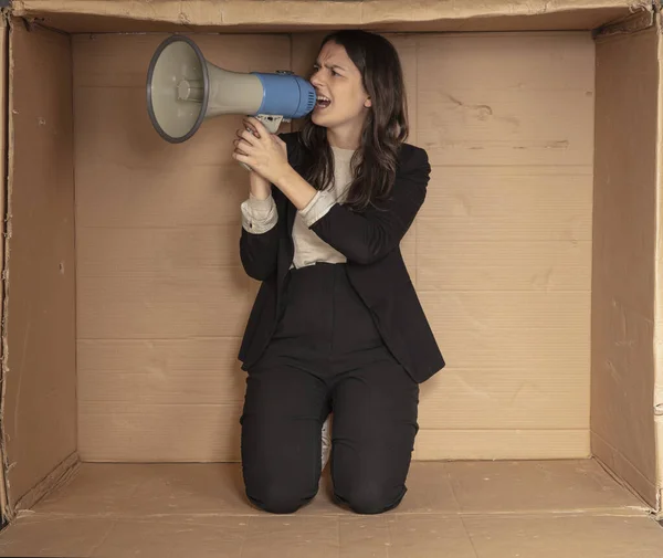 business woman with a megaphone in hand sits in a cramped cardboard office