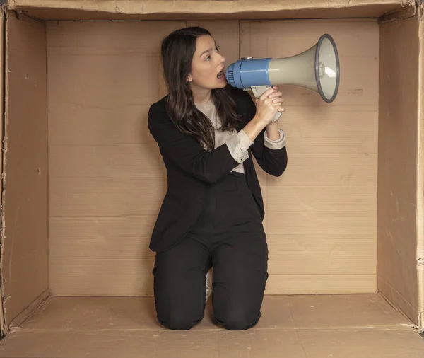 business woman with a megaphone in hand sits in a cramped cardboard office