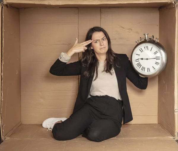 business woman with a clock in hand sits in a cardboard office