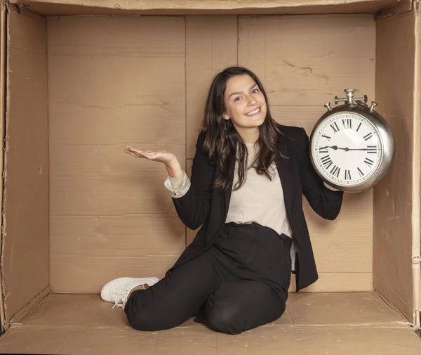 business woman with a clock in hand sits in a cardboard office