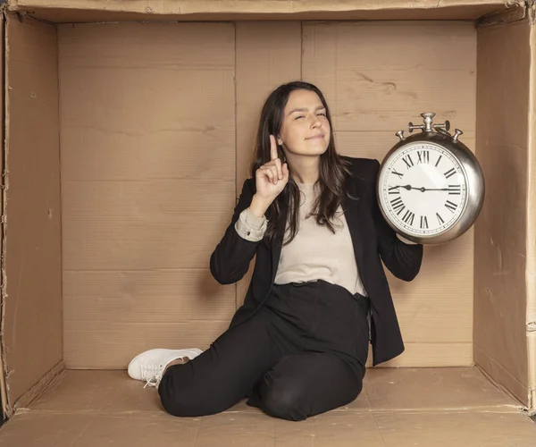 business woman with a clock in hand sits in a cardboard office