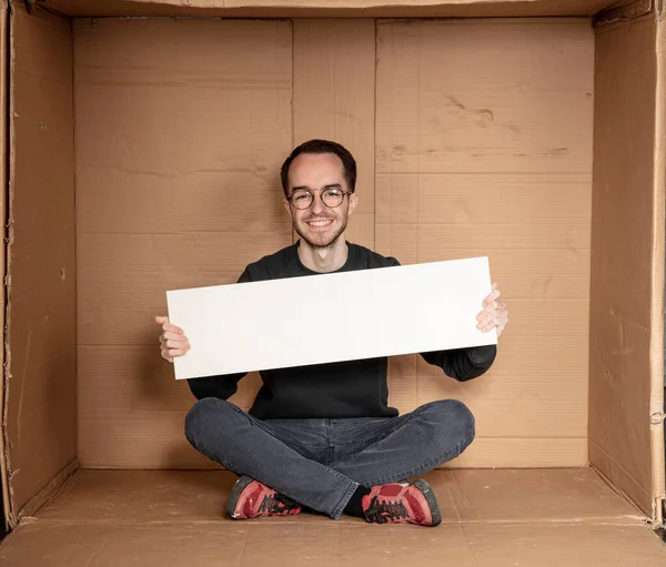 Genç işsiz bir adamın elinde beyaz bir pano, reklam için bir yer, yardım çığlığı fikri