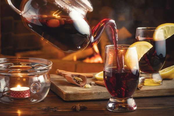 Despejando vinho quente em copos de um bule de chá em uma sala com uma lareira — Fotografia de Stock