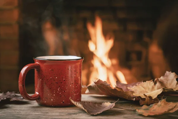 Red mug with hot tea in front of a burning fireplace, comfort and warmth of the hearth concept — Stock Photo, Image