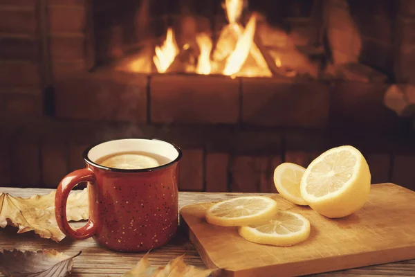 Roter Becher mit heißem Tee mit Zitrone vor dem brennenden Kamin, Komfort und Wärme des Herdkonzepts — Stockfoto
