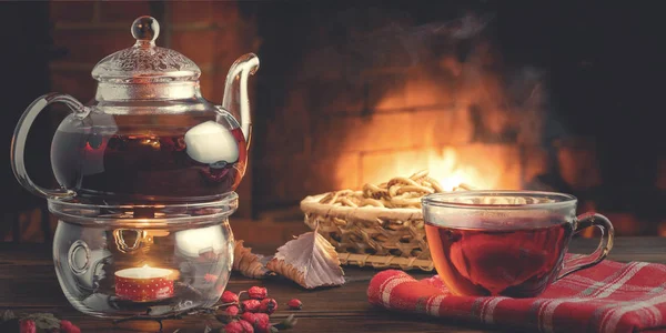 Tee mit Weißdorn in einer Glasschale und Teekanne mit Teelicht auf einem Holztisch in einem Raum mit brennendem Kamin — Stockfoto