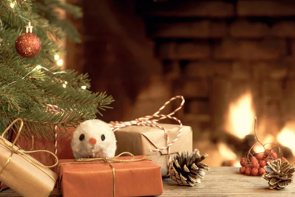 Christmas composition - mouse is symbol of 2020 according to Chinese horoscope next to gifts under Christmas tree in room by fireplace