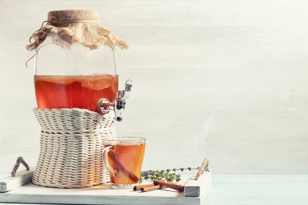 Fresh homemade kombucha fermented tea drink in a jar with faucet and in a cup on a white tray on a wooden background, copyspace