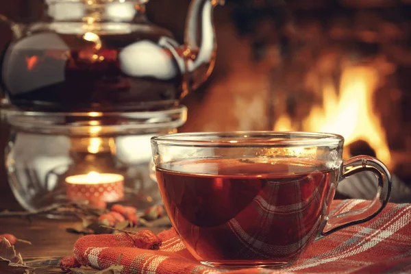 Tee mit Weißdorn in einer Glasschale und Teekanne mit Teelicht auf einem Holztisch in einem Raum mit brennendem Kamin — Stockfoto