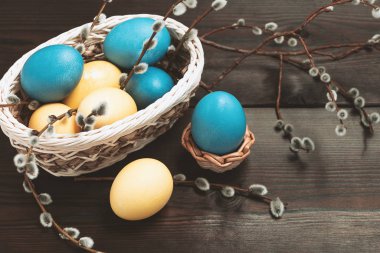 Paskalya kompozisyonu - sepetteki birkaç renkli yumurta ve söğüt dalları ile birlikte koyu ahşap bir masanın üzerinde.