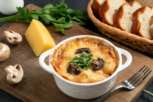 Casserole with chicken, mushrooms and cheese, known in Russia as julienne in white bowl with herbs on a wooden board, close up — Stock Image Casserole with chicken, mushrooms and cheese, known in Russia as julienne in white bowl with herbs on a wooden board, close up Royalty Free Stock Images
