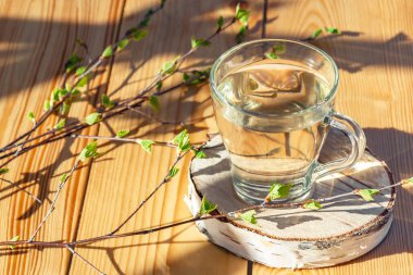 Huş ağacının dalının yanındaki cam bardakta, ahşap bir masanın üzerinde meyve suyu.
