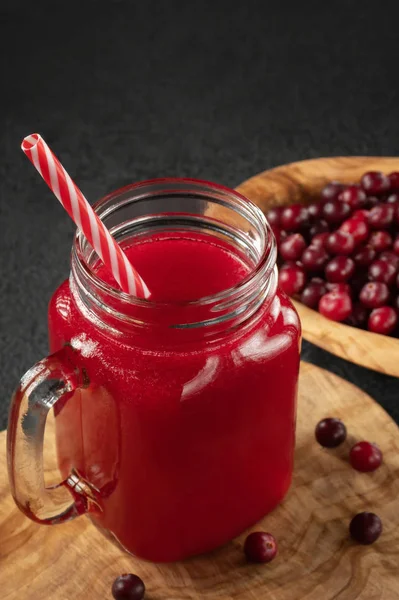 Healing cranberry juice in a glass jar-mug with a straw on black table. Healthy eating concept, vertical image — Stock Photo, Image