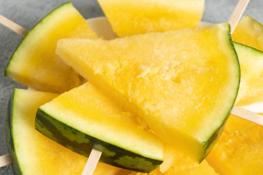 Tahta çubuklardaki sarı karpuz dilimleri yakın plan masadaki bir tabakta.