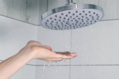 Kadın eli yağmurdan akan suya dokunuyor, su sıcaklığını kontrol ediyor.