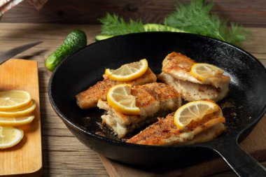 Siyah dökme demir bir tavada, taze salatalık ve bitkilerle porsiyonlu balık parçaları. Köy balıkçısının geleneksel yemeği.