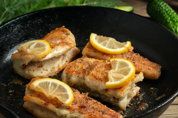 Portioned pieces of fried fish in a black cast-iron pan with fresh cucumbers and herbs. Traditional dinner of a village fisherman — Stock Photo, Image