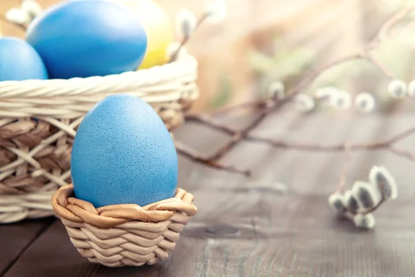 Easter composition - several colored eggs in a basket and on a dark wooden table with willow twigs — Stock Photo, Image