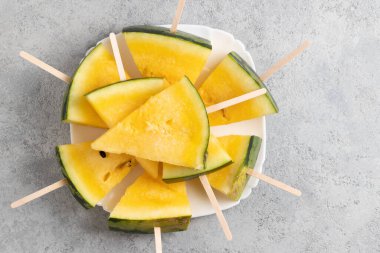 Sarı karpuz dilimleri ahşap çubuklar üzerinde masada bir tabakta
