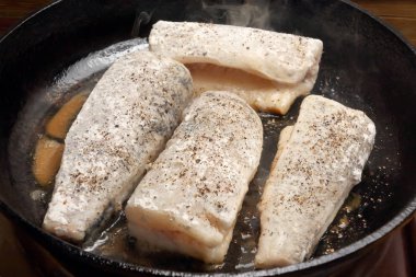 Siyah dökme bir tavada taze balık parçaları kızartıyorlar.