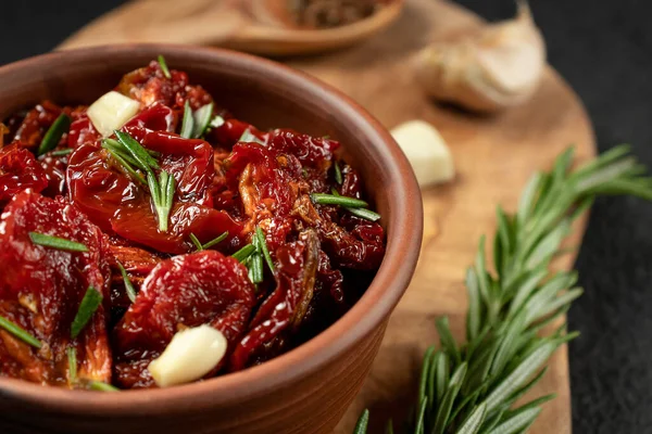 Tomates secados al sol con ajo, romero y especias en un tazón de barro sobre una tabla de cortar de madera de olivo — Foto de Stock