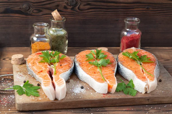 Three raw salmon steaks on a wooden cutting board prepared for cooking — Stock Photo, Image