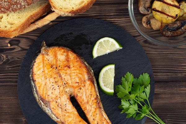 Grilled salmon steak on a black slate dish with parsley and lime — Stock Photo, Image
