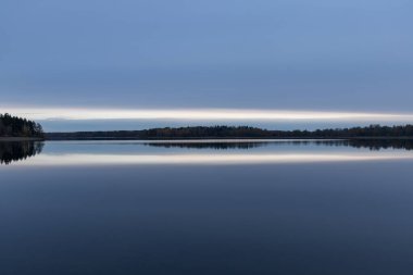 Huzurlu bir manzara. Gölde gün batımı, sakin su yüzeyi, simetrik yansıma.